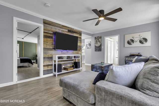 living room with an accent wall, wood finished floors, baseboards, and ceiling fan
