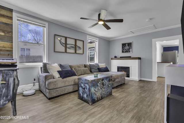 living area with a warm lit fireplace, wood finished floors, crown molding, and ceiling fan