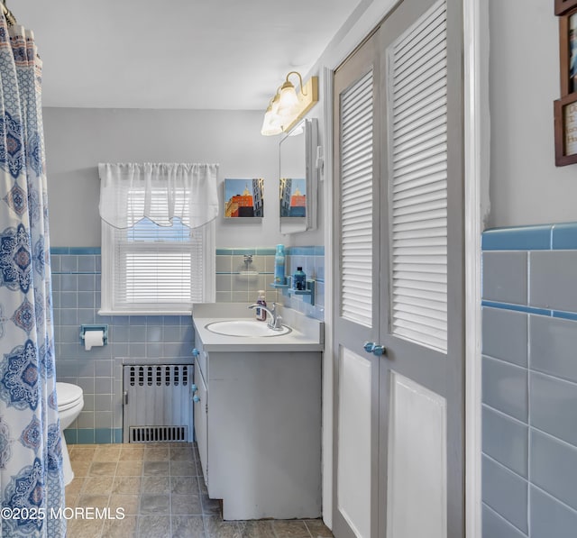 full bath with radiator, toilet, vanity, tile walls, and wainscoting