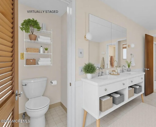 bathroom featuring toilet, a sink, double vanity, and baseboards