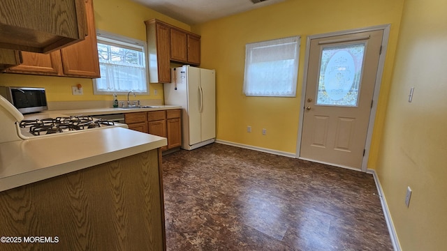 kitchen with brown cabinetry, baseboards, a sink, and white appliances