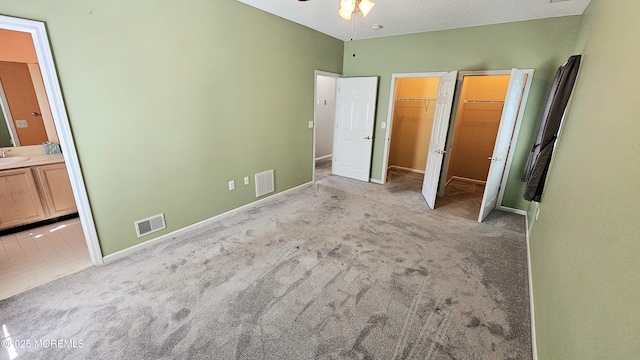 unfurnished bedroom with a spacious closet, ensuite bath, visible vents, and carpet