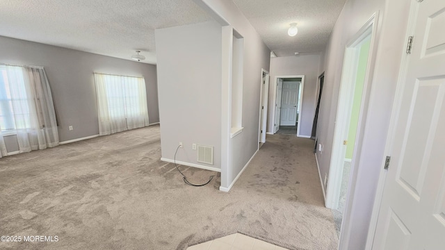 hall with a textured ceiling, carpet, visible vents, and baseboards