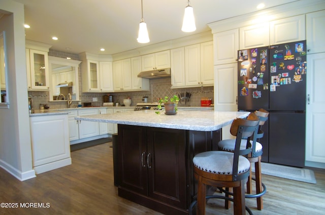 kitchen featuring backsplash, white cabinets, freestanding refrigerator, a breakfast bar, and dark wood-type flooring