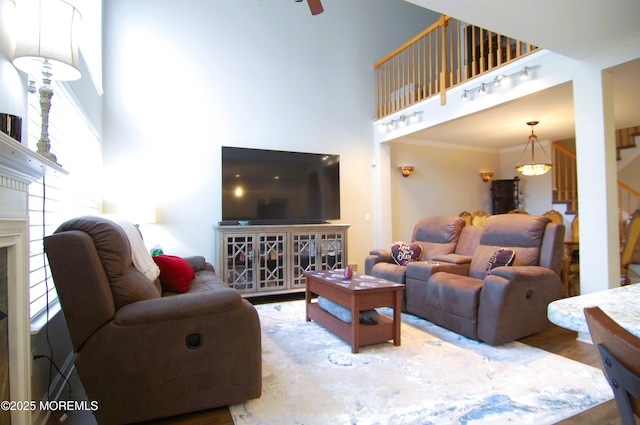 living area with crown molding, a high ceiling, a fireplace, wood finished floors, and stairway