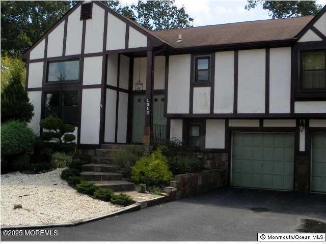 tudor-style house featuring stucco siding, aphalt driveway, and a garage