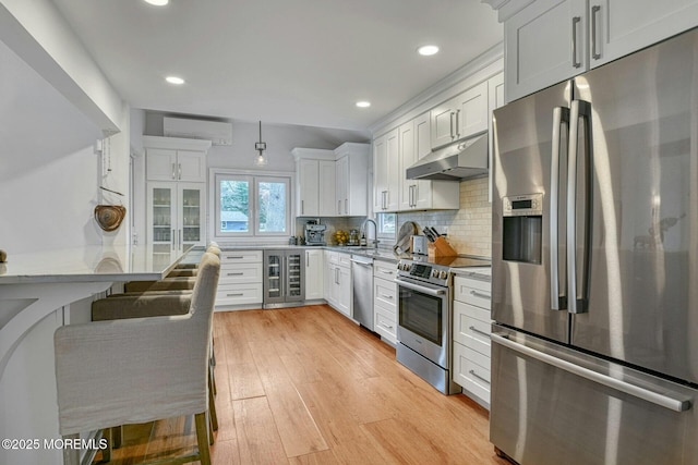 kitchen with stainless steel appliances, under cabinet range hood, a wall mounted AC, white cabinetry, and wine cooler