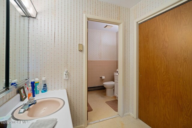 bathroom with a baseboard radiator, toilet, vanity, and wallpapered walls