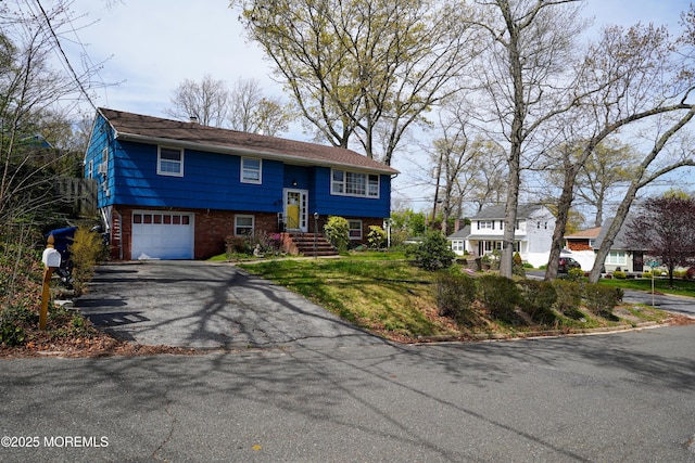 raised ranch featuring brick siding, a garage, and aphalt driveway