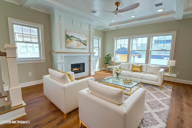 living area with ceiling fan, hardwood / wood-style floors, a glass covered fireplace, baseboards, and beam ceiling