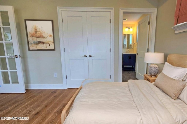 bedroom with baseboards, a closet, wood finished floors, and connected bathroom
