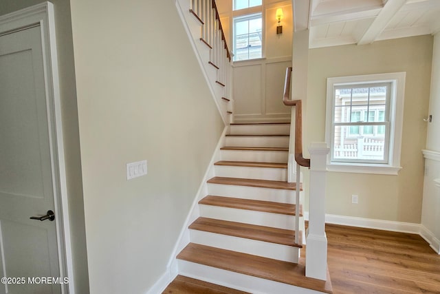 stairway with wood finished floors, beamed ceiling, and baseboards