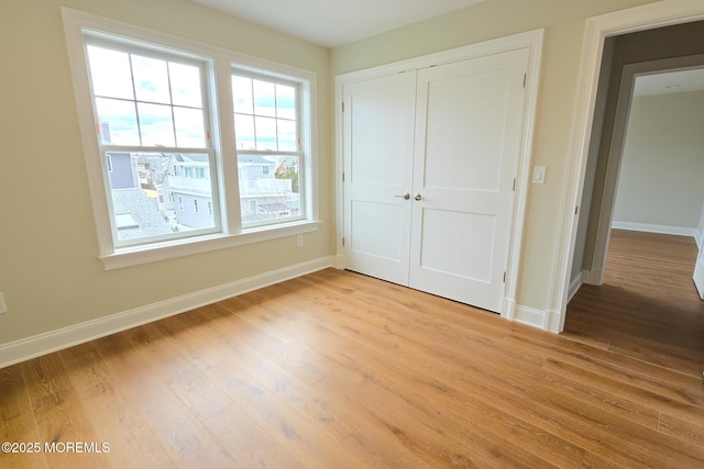 unfurnished bedroom featuring baseboards, light wood finished floors, and a closet