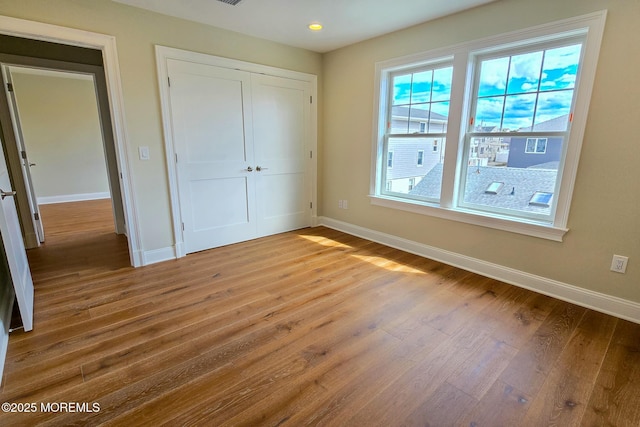 unfurnished bedroom with wood finished floors, baseboards, a closet, and recessed lighting