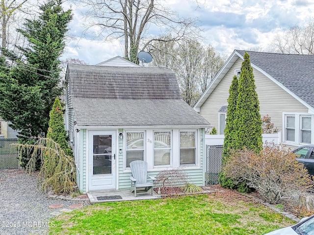 view of front facade featuring fence, roof with shingles, and a front yard
