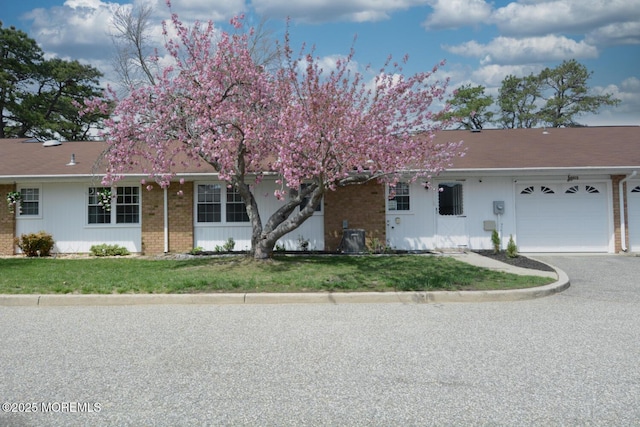 single story home featuring a front lawn, driveway, a garage, and brick siding
