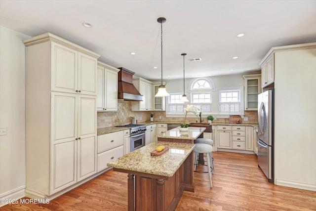 kitchen featuring stainless steel appliances, visible vents, a kitchen island, glass insert cabinets, and custom range hood