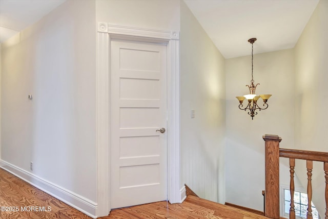 hallway with baseboards, a notable chandelier, an upstairs landing, and light wood-style flooring