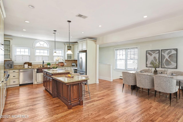 kitchen with a kitchen breakfast bar, stainless steel appliances, a kitchen island, and light wood-style flooring