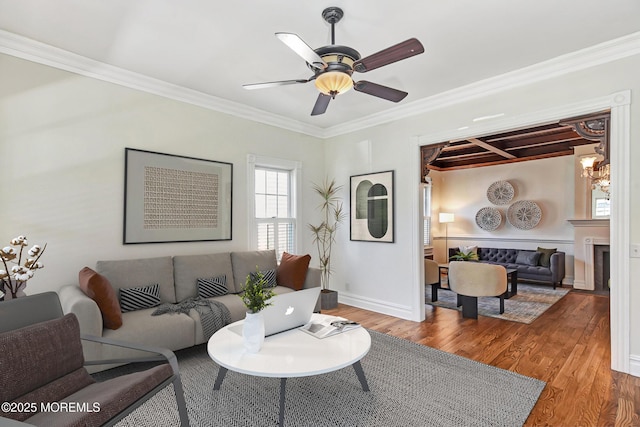 living room featuring wood finished floors, crown molding, baseboards, and ceiling fan with notable chandelier