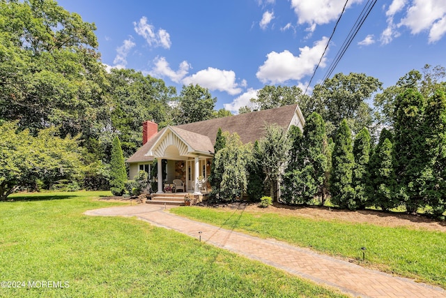 view of front of home with a front lawn, a shingled roof, a porch, and a chimney