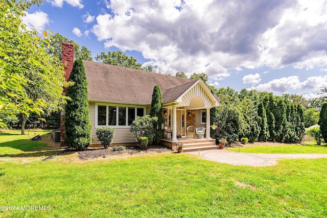 bungalow-style house with a chimney, cooling unit, a porch, and a front lawn