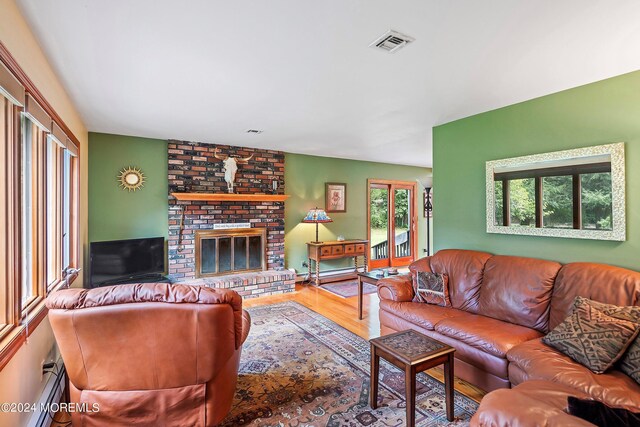 living area featuring a brick fireplace, wood finished floors, visible vents, and a baseboard heating unit