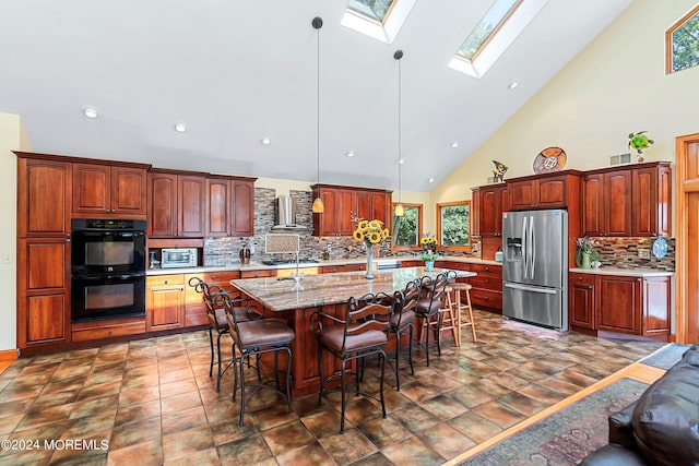 kitchen with stainless steel fridge, a kitchen bar, a skylight, dobule oven black, and wall chimney range hood