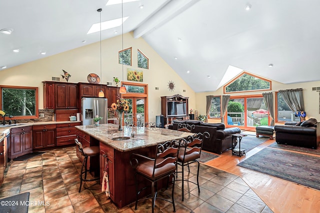 kitchen with a sink, a skylight, stainless steel refrigerator with ice dispenser, high vaulted ceiling, and open floor plan