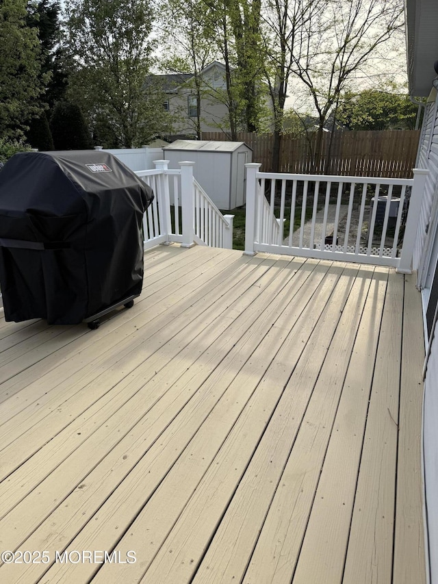 deck featuring an outdoor structure, a fenced backyard, a shed, and a grill