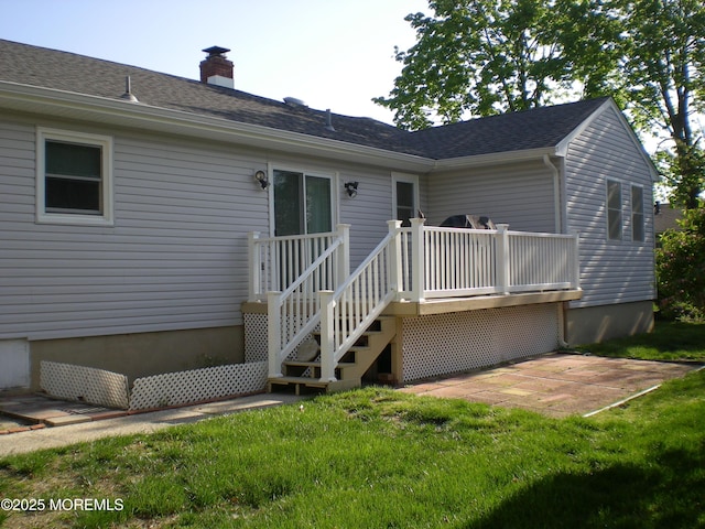 back of property with a chimney, a lawn, roof with shingles, and a deck