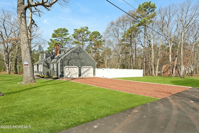 exterior space featuring a lawn, a chimney, dirt driveway, an attached garage, and fence