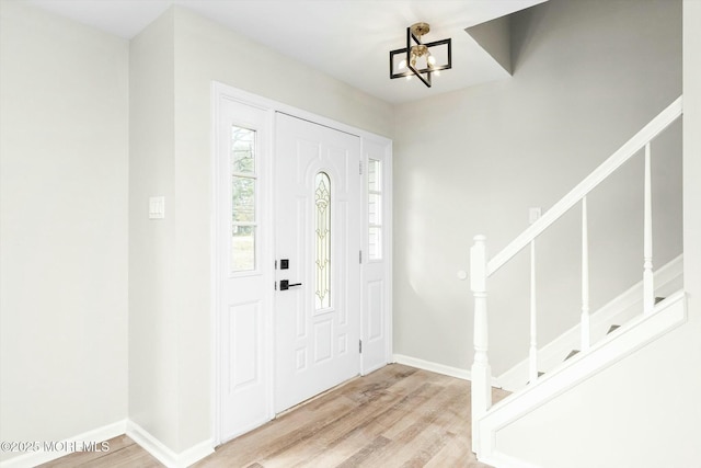 foyer featuring baseboards, wood finished floors, an inviting chandelier, and stairway