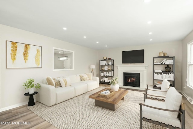 living room with recessed lighting, a glass covered fireplace, wood finished floors, and baseboards