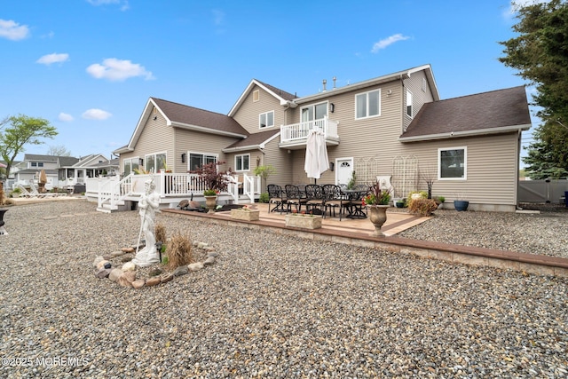 rear view of property featuring roof with shingles, a patio area, a balcony, and a wooden deck
