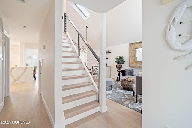 stairway with a towering ceiling, a skylight, wood finished floors, and baseboards