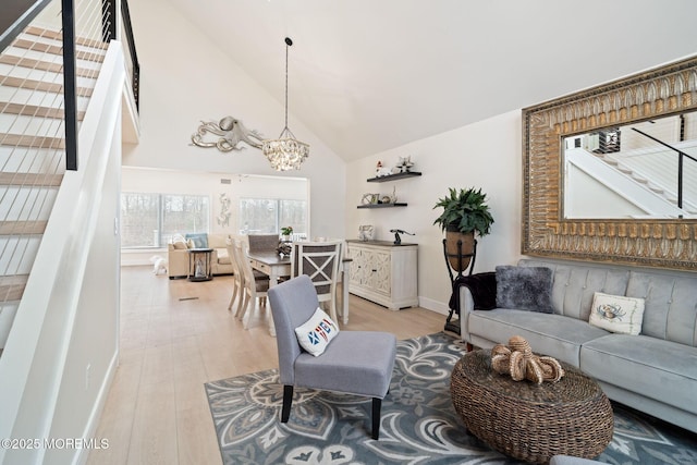living room with a notable chandelier, light wood-type flooring, high vaulted ceiling, and baseboards