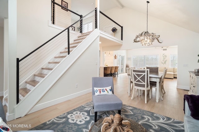 interior space featuring stairs, baseboards, light wood-type flooring, a notable chandelier, and high vaulted ceiling
