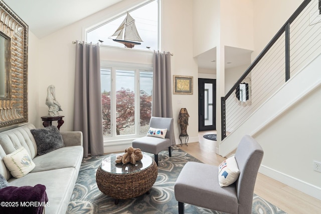 living room featuring baseboards, high vaulted ceiling, wood finished floors, and stairs