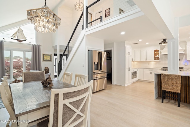 dining area featuring recessed lighting, an inviting chandelier, light wood-style flooring, stairway, and a towering ceiling