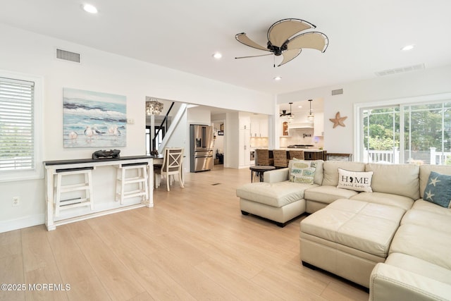 living area featuring stairway, visible vents, a ceiling fan, and light wood finished floors