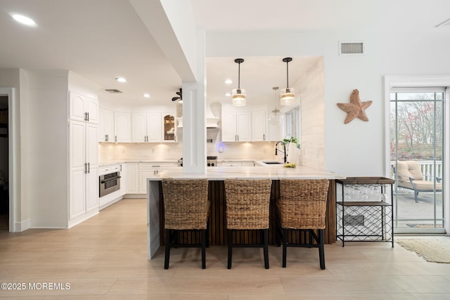 kitchen featuring a sink, a breakfast bar, a peninsula, stainless steel oven, and backsplash