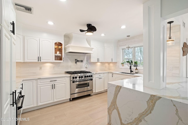 kitchen featuring high end stove, a sink, visible vents, premium range hood, and white cabinets