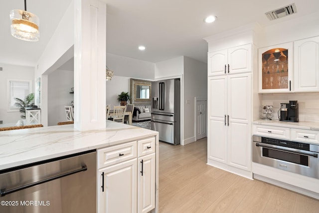 kitchen with glass insert cabinets, light stone counters, appliances with stainless steel finishes, light wood-type flooring, and visible vents