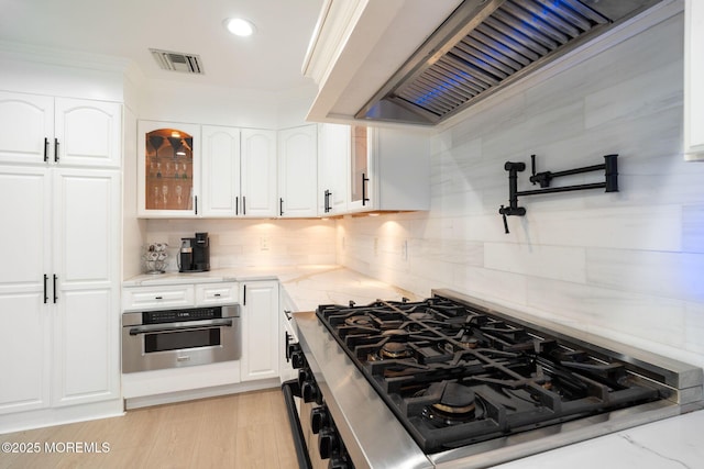 kitchen with white cabinetry, stovetop, oven, light stone countertops, and custom exhaust hood