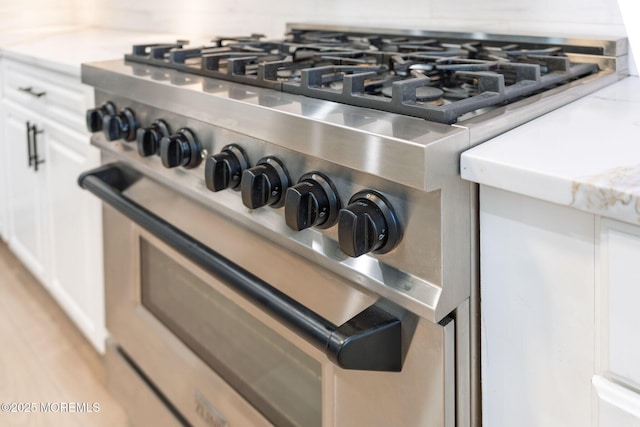 details with high end range, white cabinets, backsplash, and light wood-style floors