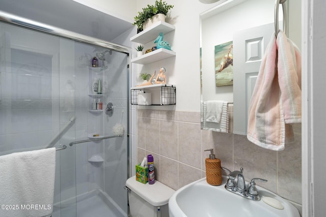 bathroom with tile walls, backsplash, toilet, a sink, and a stall shower