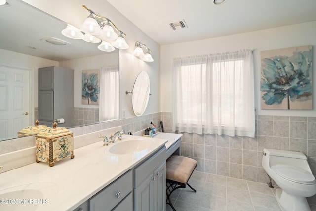 bathroom with tile walls, visible vents, toilet, and a sink