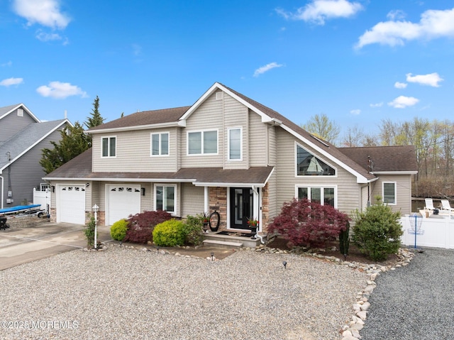 traditional-style house with a shingled roof, stone siding, concrete driveway, an attached garage, and fence