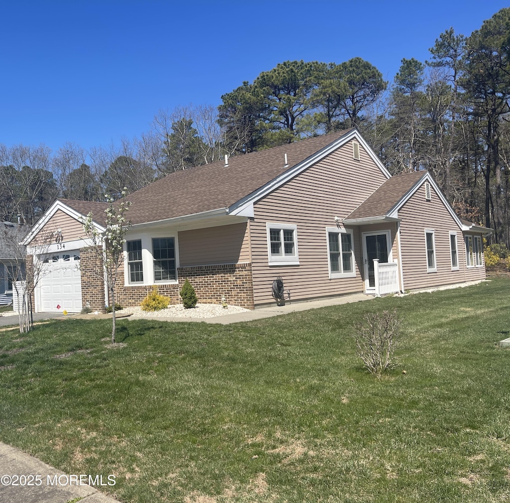 ranch-style home featuring a front lawn, roof with shingles, a garage, and brick siding